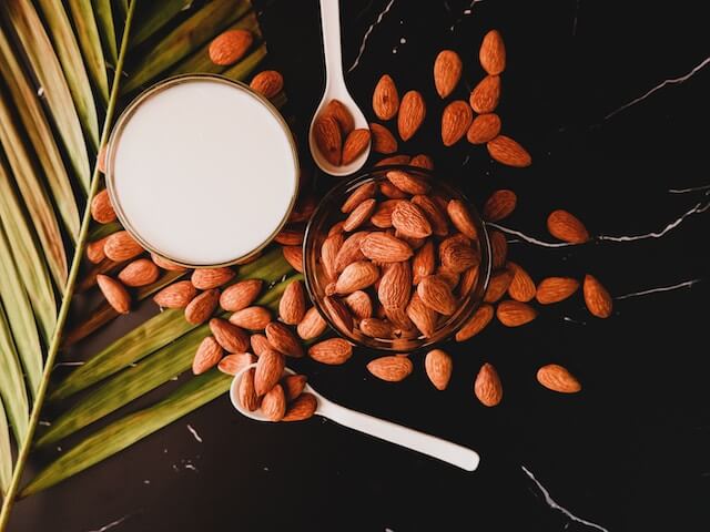 A glass of milk and almonds on a tableDescription automatically generated