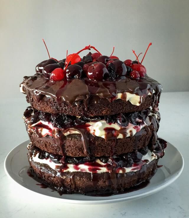A cake with chocolate frosting and cherries on topDescription automatically generated