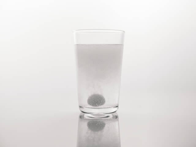 A glass of water with a pill in itDescription automatically generated