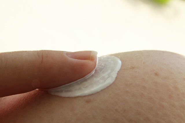 A person applying a white cream on their skinDescription automatically generated