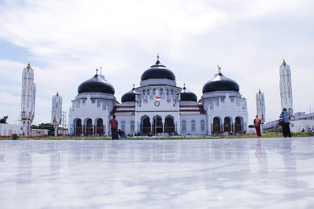 A large white building with black domes with Baiturrahman Grand Mosque in the backgroundDescription automatically generated
