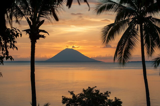 A sunset over a body of water with a mountain in the distanceDescription automatically generated