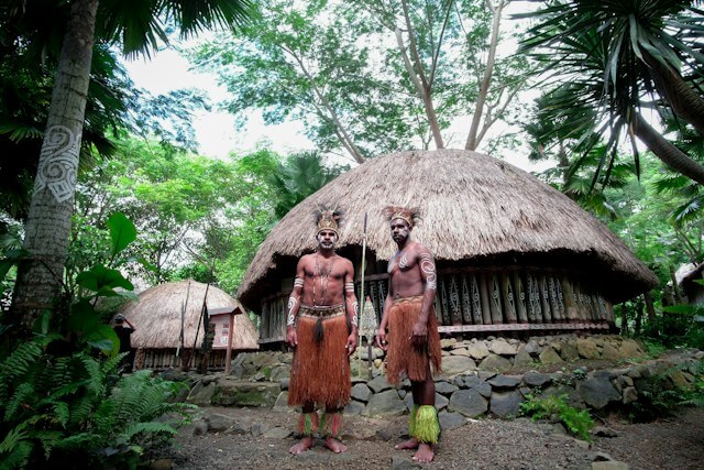 Men in traditional attire standing in front of a hutDescription automatically generated