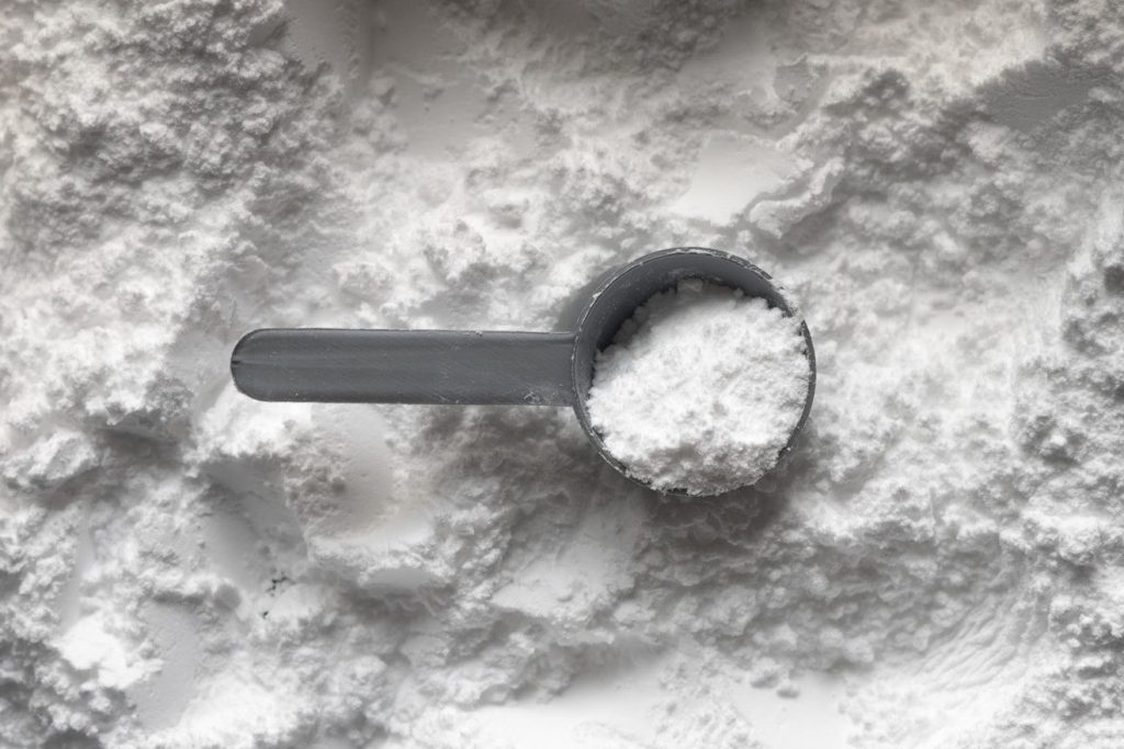 A grey plastic scoop filled with white powder resting on a pile of powder